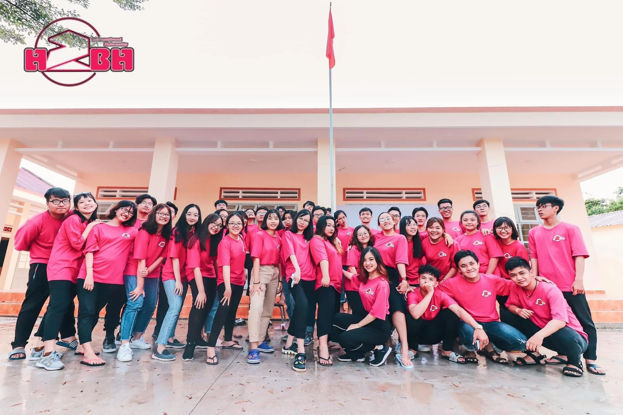 Group of young people wearing matching pink shirts, standing in front of a building, posing for a group photo.