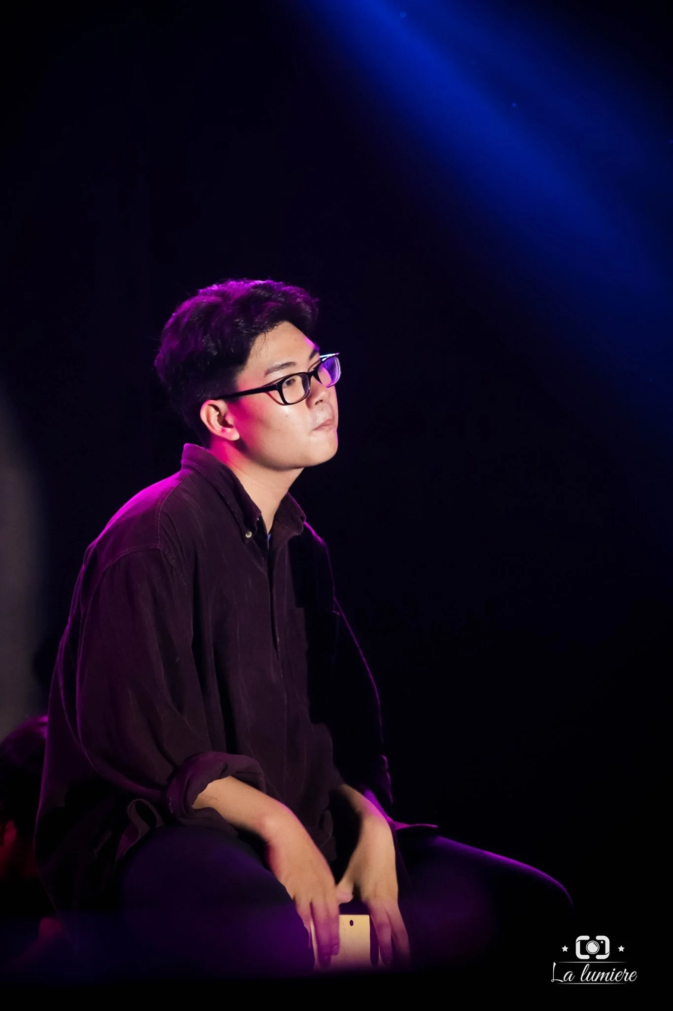 Young man with glasses sitting on a chair in a dark room illuminated by purple and blue lights