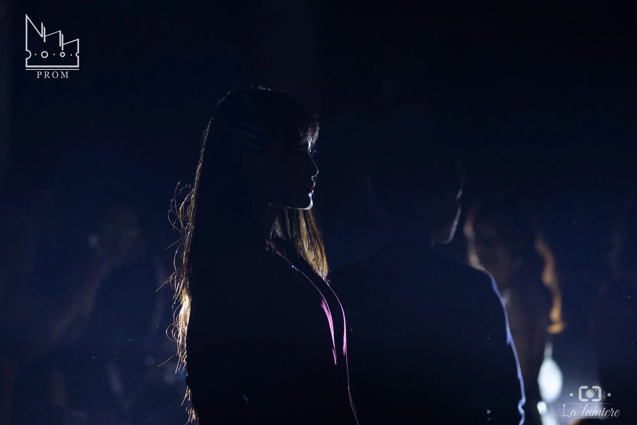 Silhouette of a woman at night with a dark background, several other silhouettes are visible in the background.