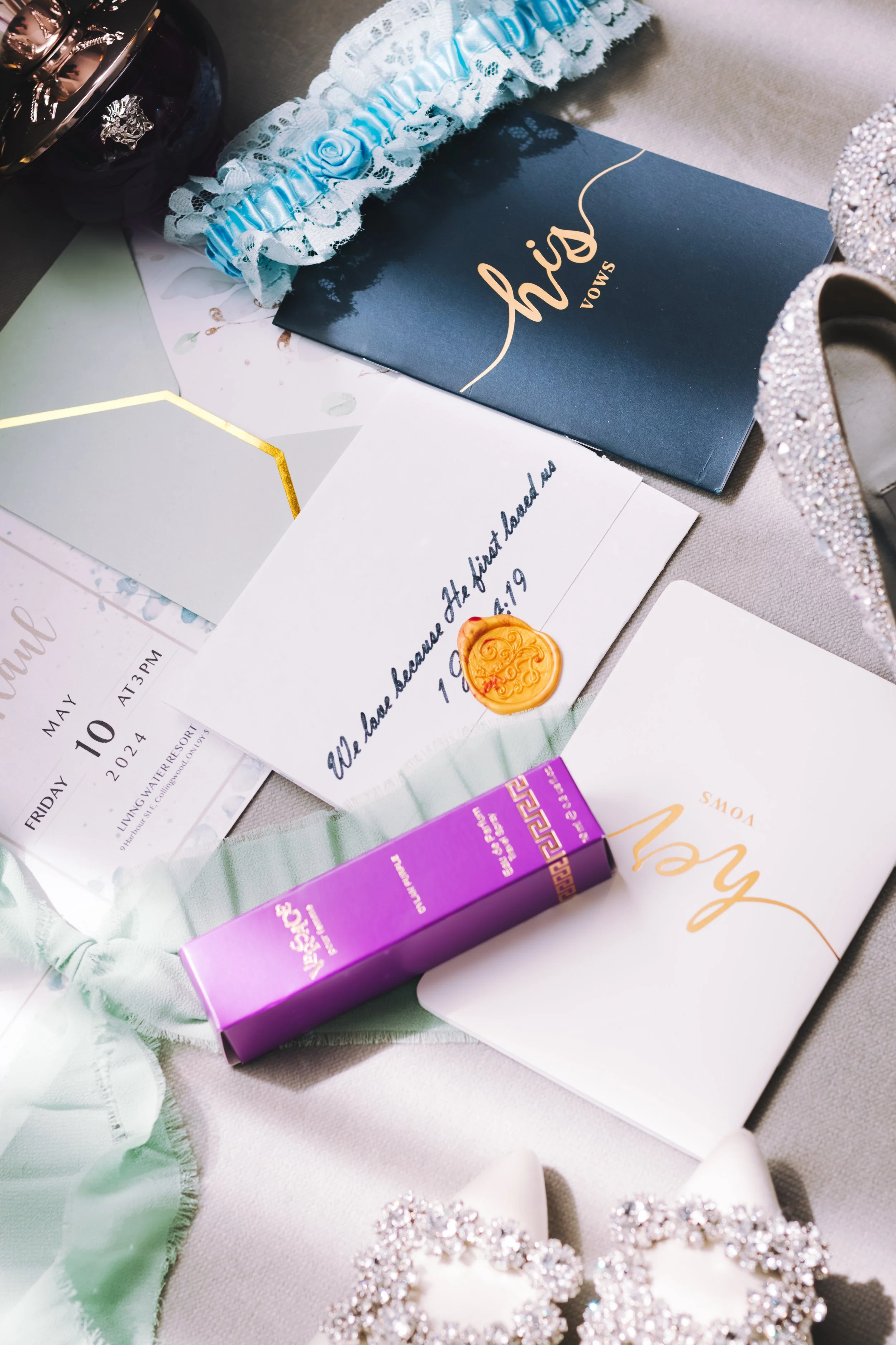 Wedding invitation, cards, and accessories including shoes, a garter, and a candle on a table