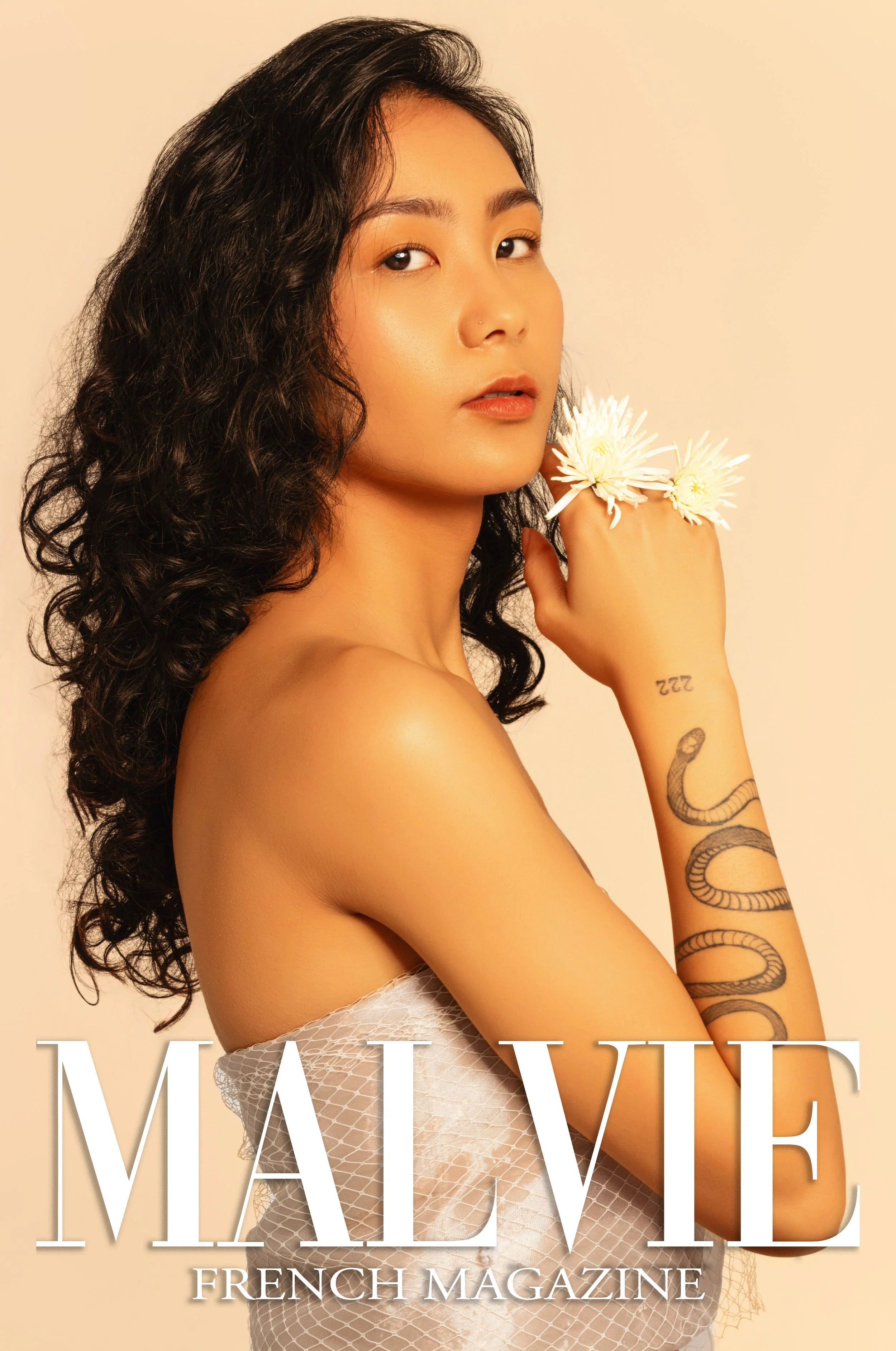 Cover of Malve French magazine featuring a woman with curly hair holding flowers near her face, with tattoos on her arm, wearing a textured, sleeveless top, and looking at the camera.