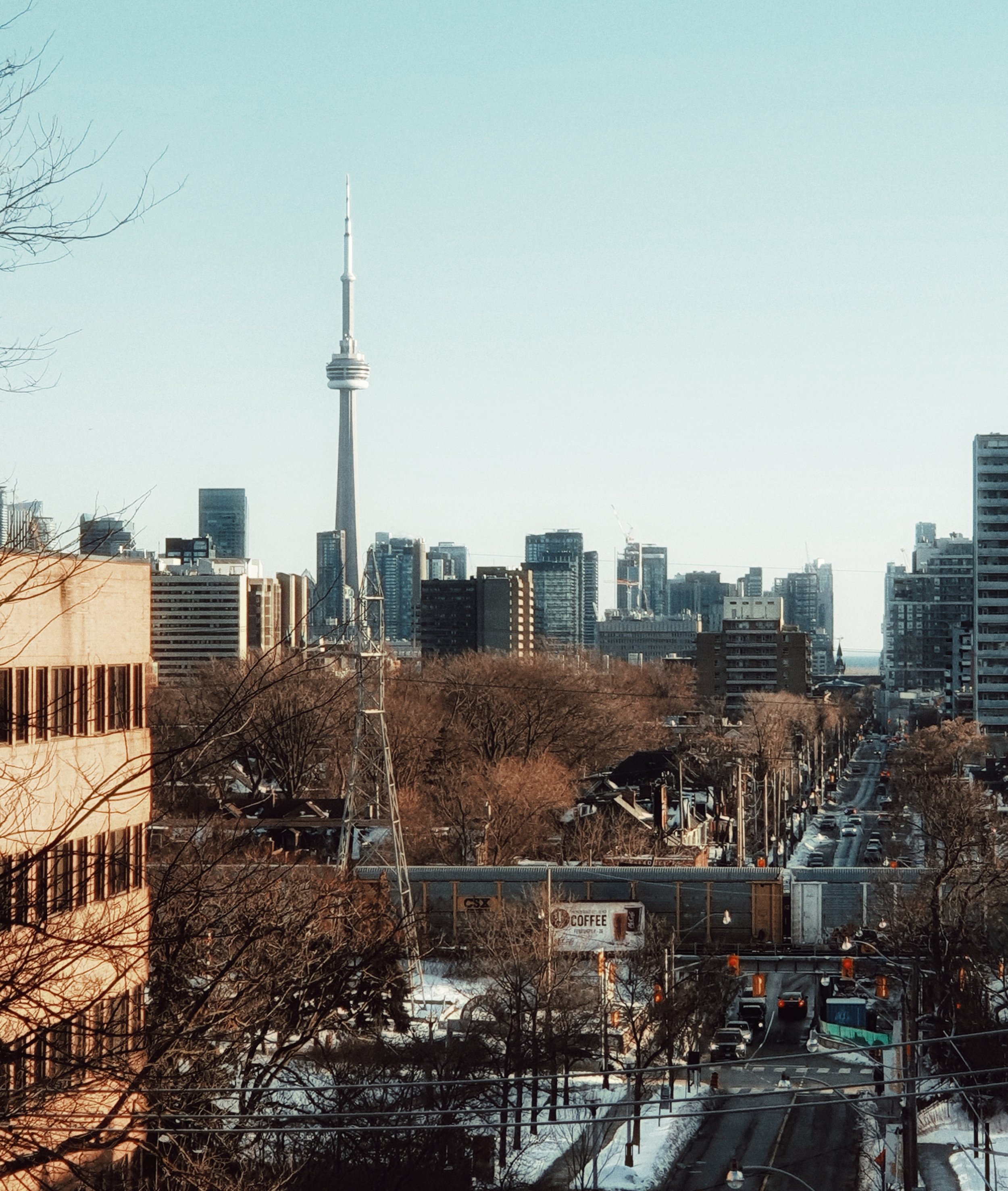 City skyline with CN Tower visible, snow on the ground, and traffic on a main road.