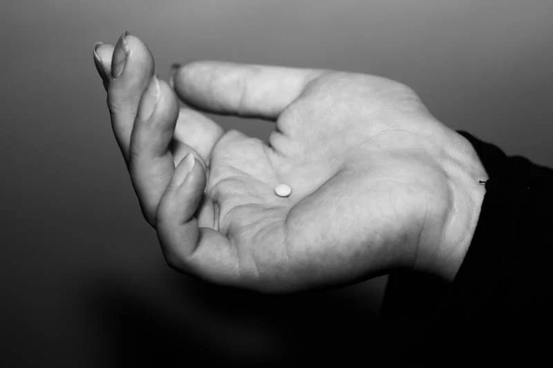 Black and white image of an open hand holding a small pill.