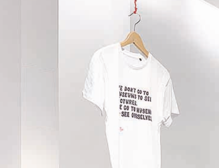 White T-shirt hanging on a wooden hanger, with black text printed on the front.