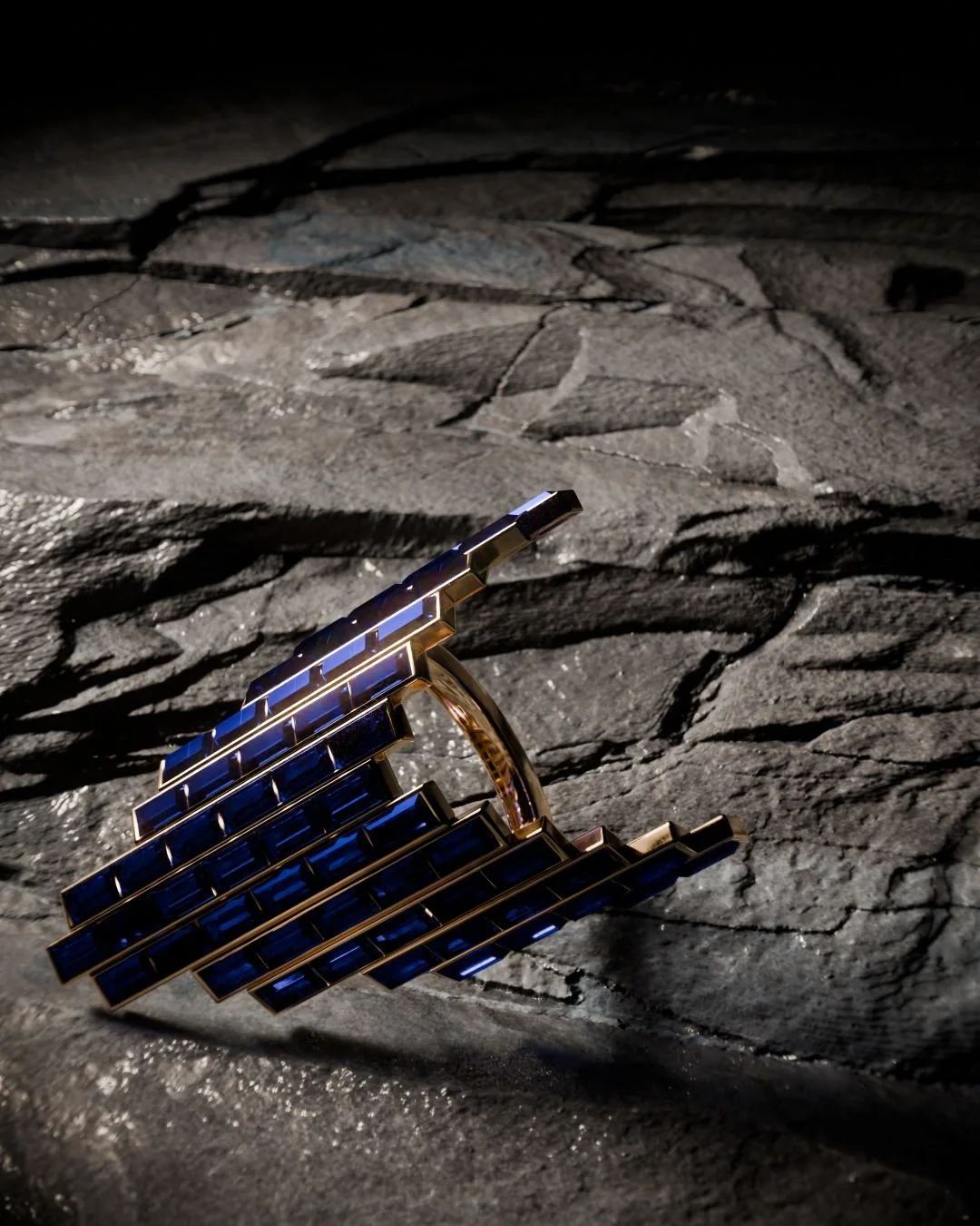 Close 3D render of deep-blue baguette stones set in gold on a fissured dark stone surface.
