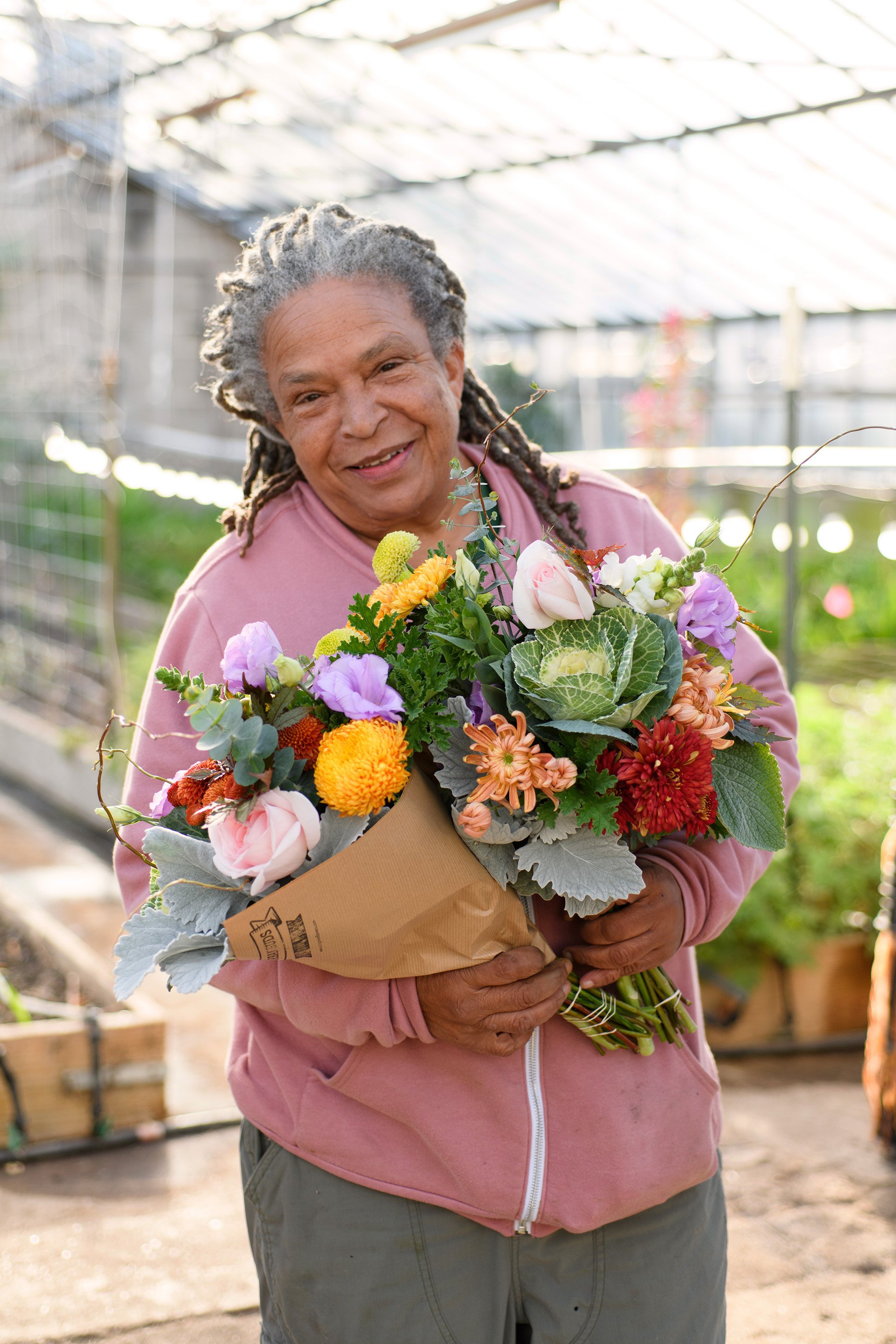 Flower farmer holding a bouquet of colorful flowers inside a greenhouse.