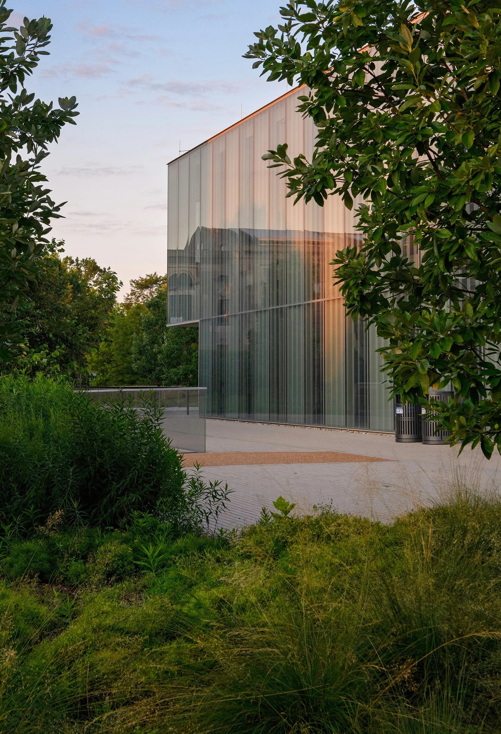 Modern glass building surrounded by greenery and trees during daytime.
