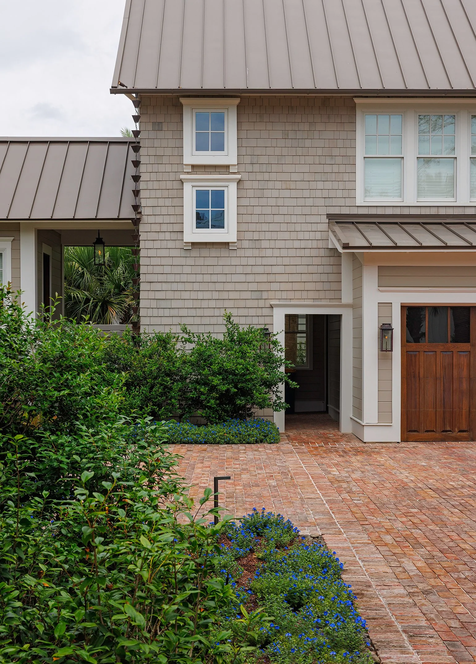 Front view of a house with a brick driveway, green bushes, and a wooden garage door.