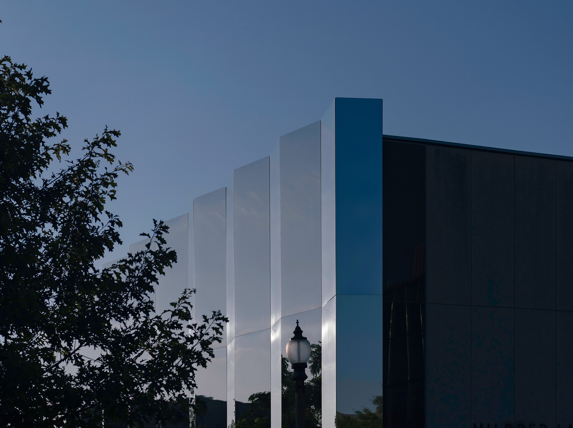 Modern building with reflective glass panels and trees in foreground during daytime.