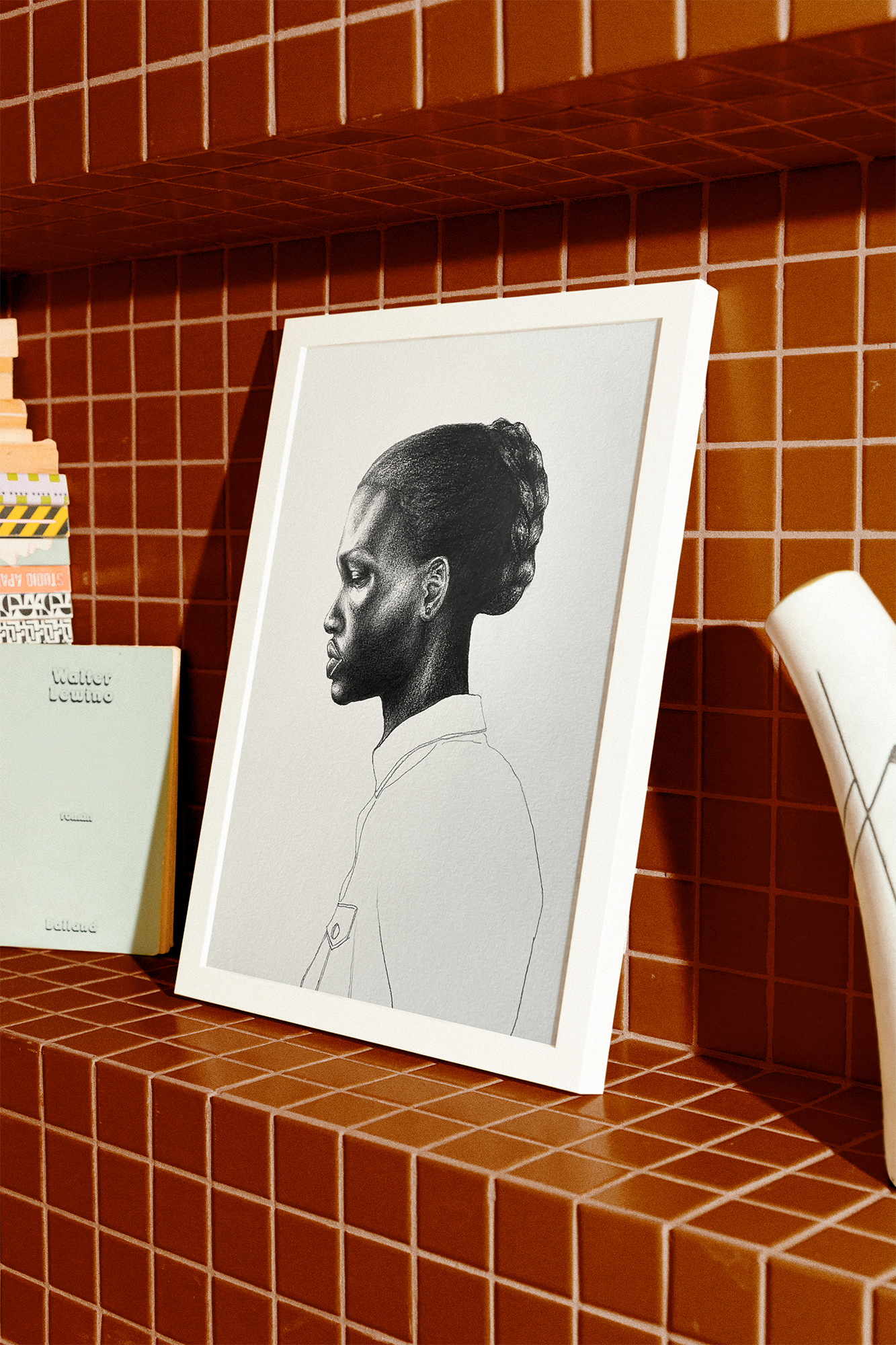 A framed black and white profile drawing of a woman with natural hair styled in an updo, placed on a red tiled shelf.