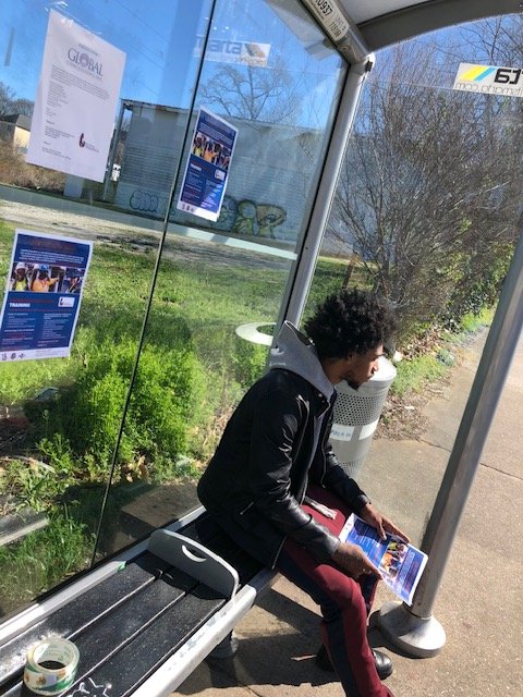 A community member pictured at a Marta bus stop hanging up signs sharing communtiy resources.