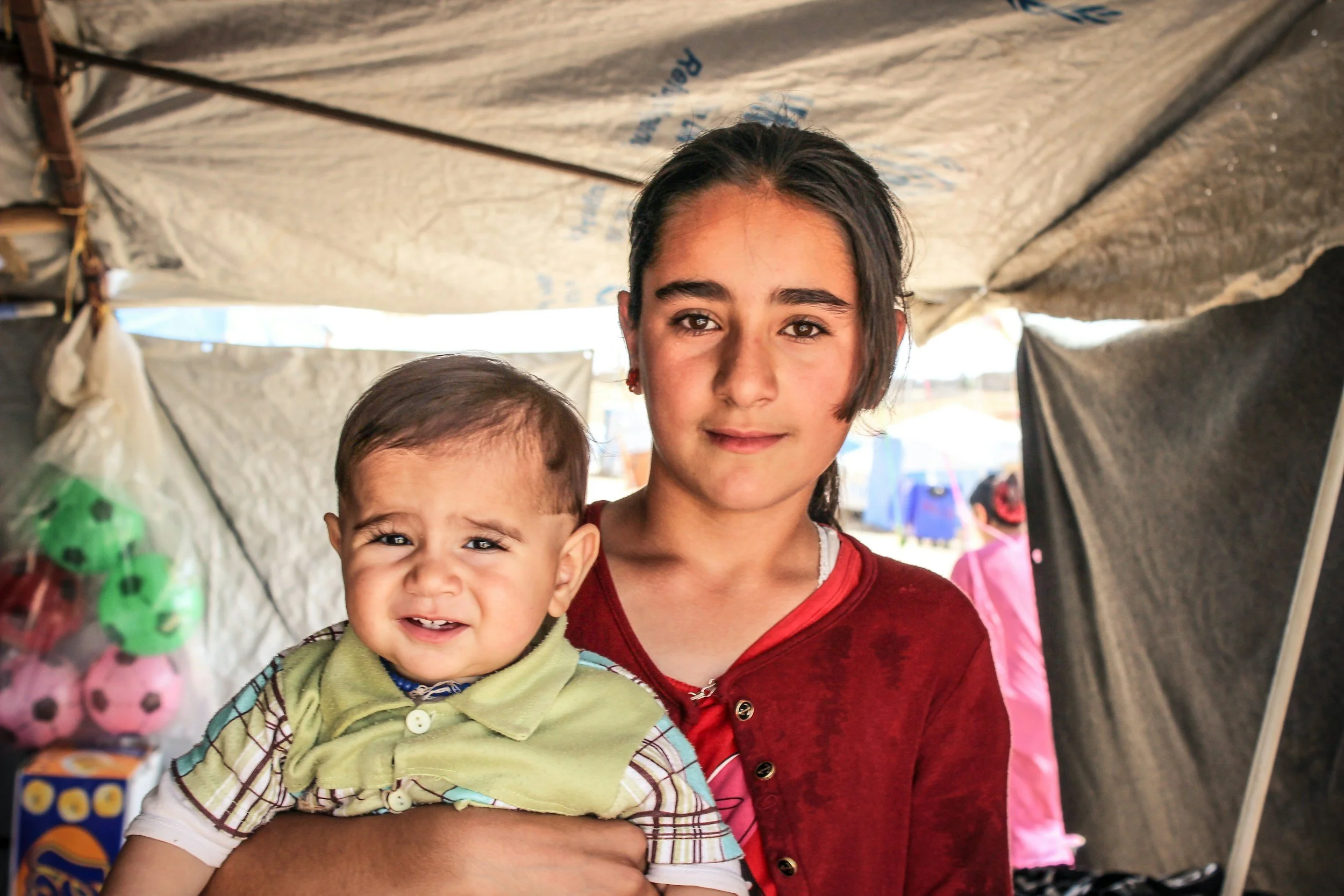 Refugee woman holding infant boy standing in temporary tent accommodation