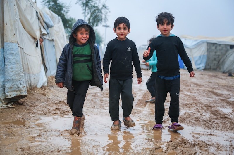 Three young boys walking through muddy refugee camp