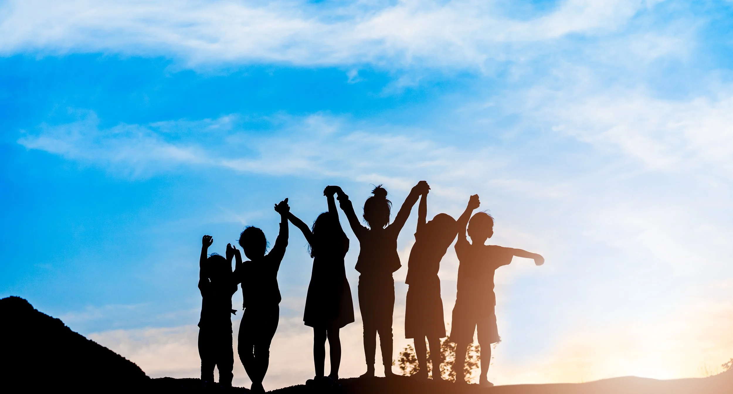 Group of children holding hands in silhouette against a blue sky