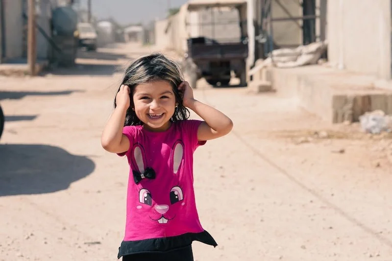 Young refugee girl holding back hair wearing pink t-shirt with rabbit face