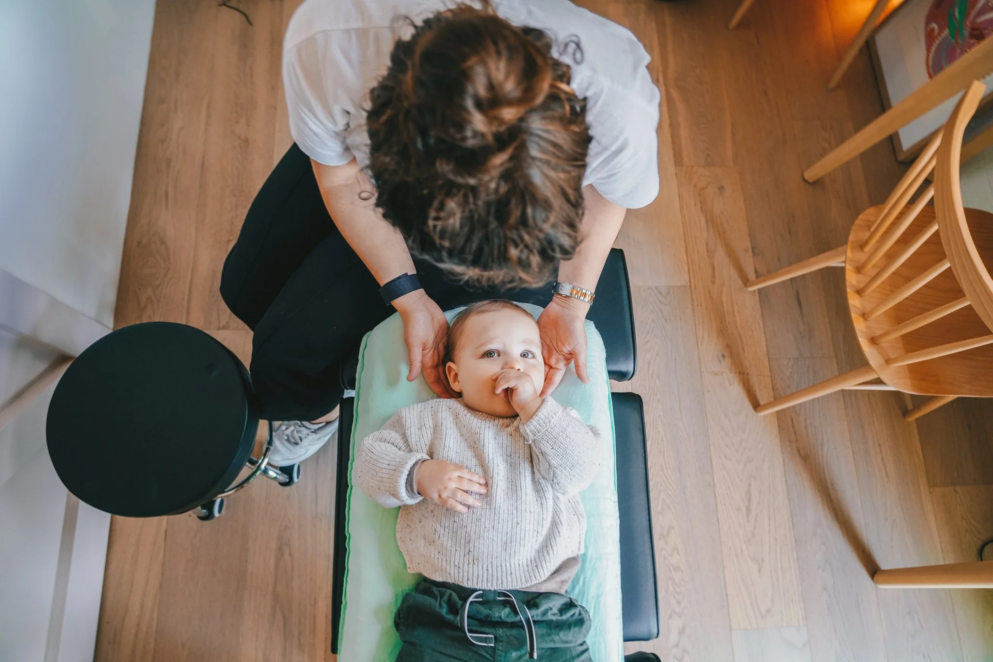 A toddler lying on a changing table getting their neck checked by a healthcare professional, viewed from above.