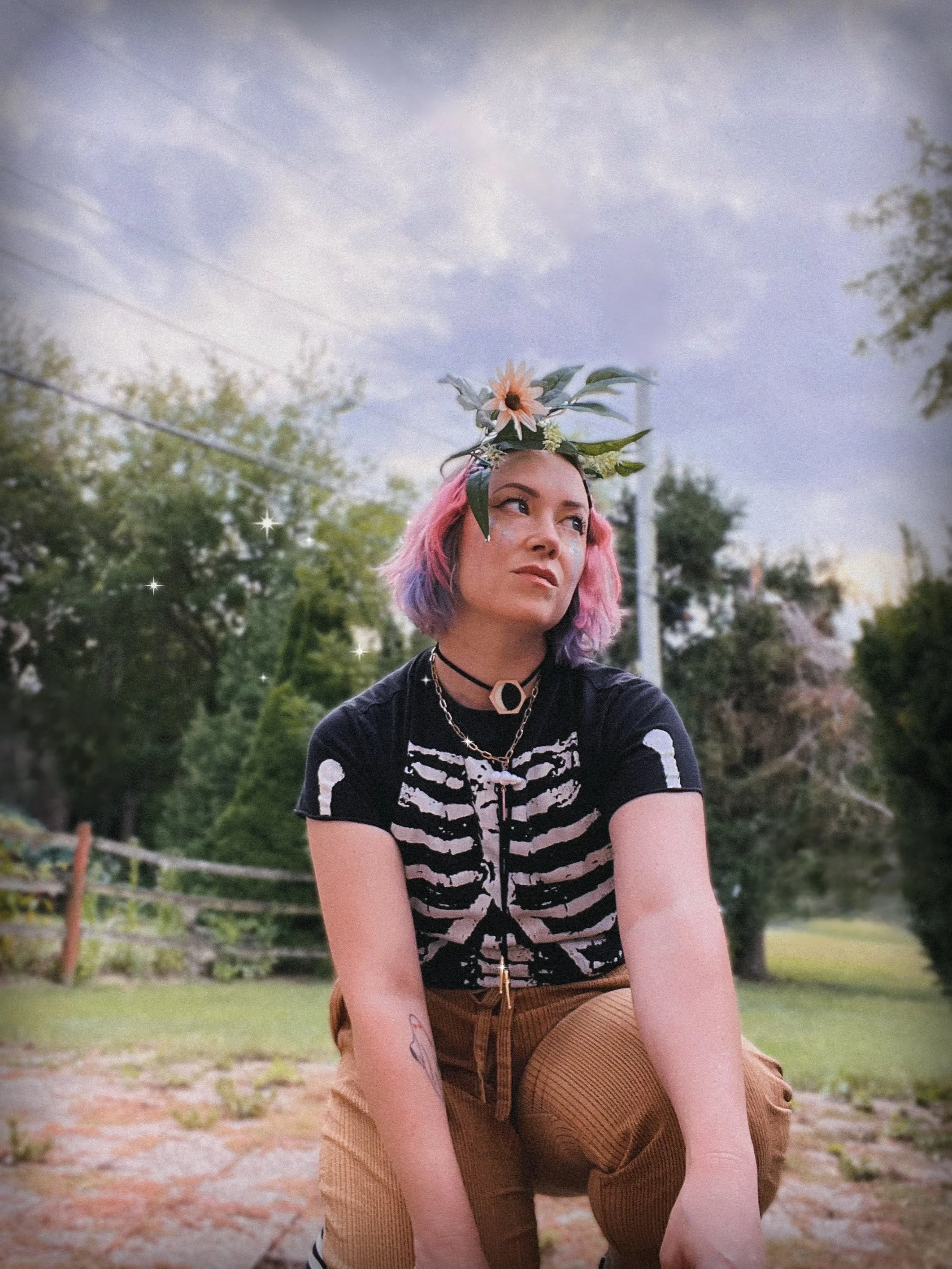 Picture of the artist, Karlee Beth Barr in her yard with a floral headpiece and a skeleton tee.