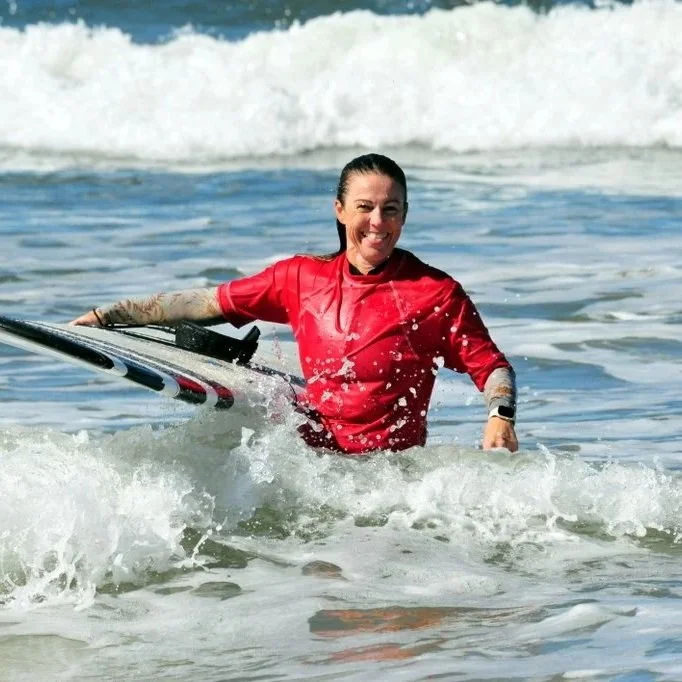 OBMC happy female longboarder holding a surfboard, smiling in the ocean with waves.