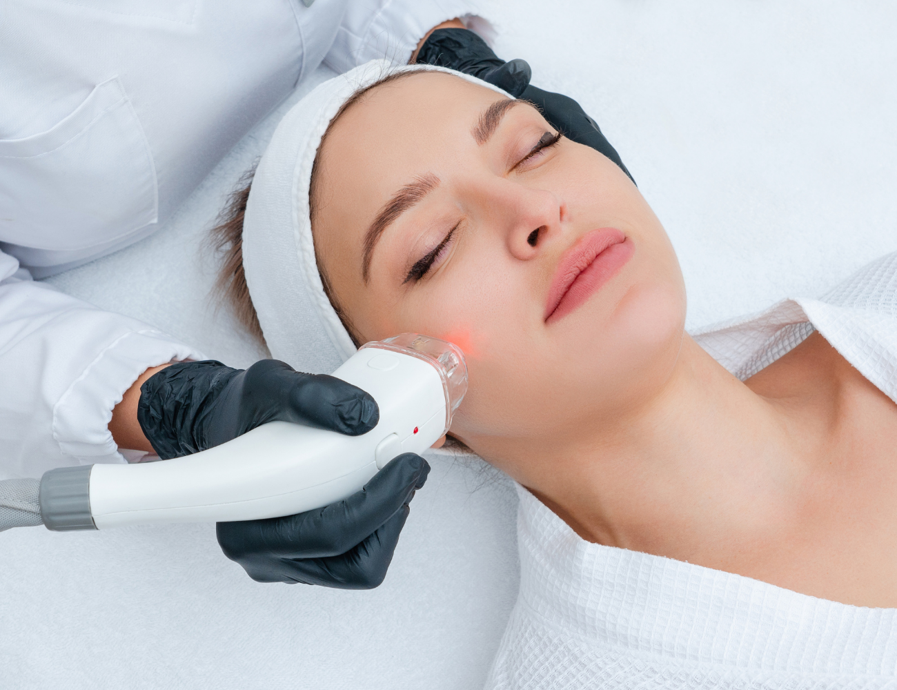 A woman receiving a skin treatment with a handheld device applied to her face in a clinical setting.