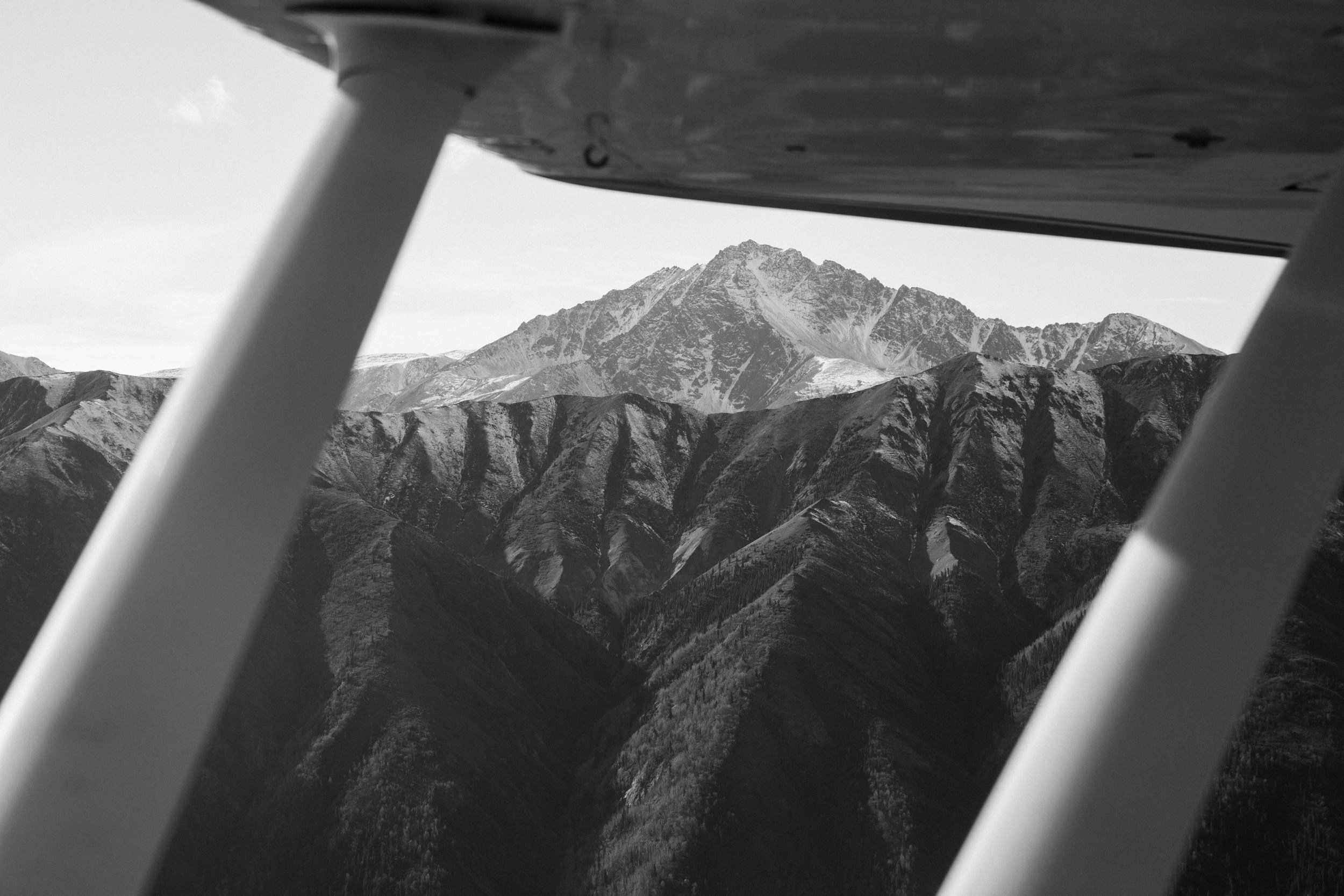 View of snow-capped mountain peaks through the window of an aircraft, with the airplane cabin structure in the foreground.