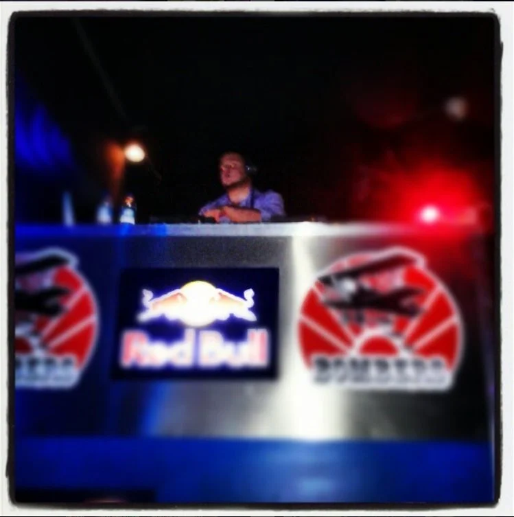 DJ Molex at a Red Bull-sponsored event with Red Bull logos on the DJ booth, dark background, and colorful lights.