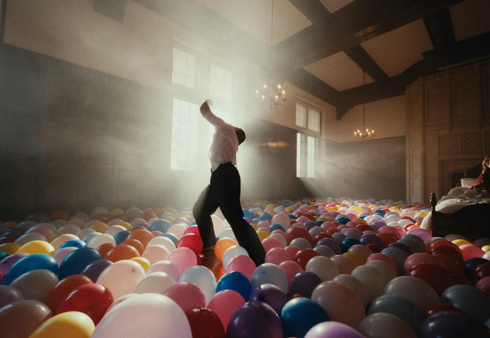 Person dancing in a room filled with colorful balloons, with sunlight streaming through large windows.