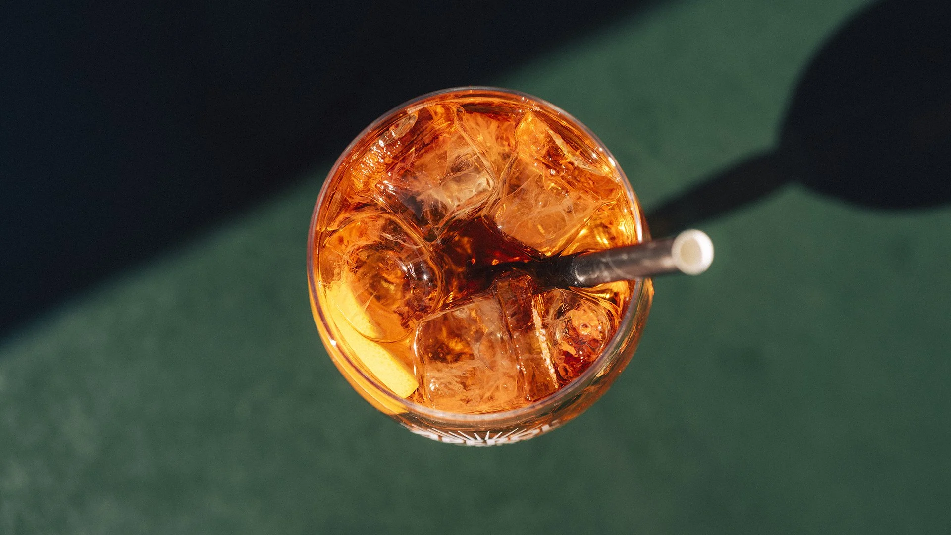 Ein Glas mit Eiswürfeln und einem dunklen Getränk, dazu ein Strohhalm und eine Zitronenscheibe