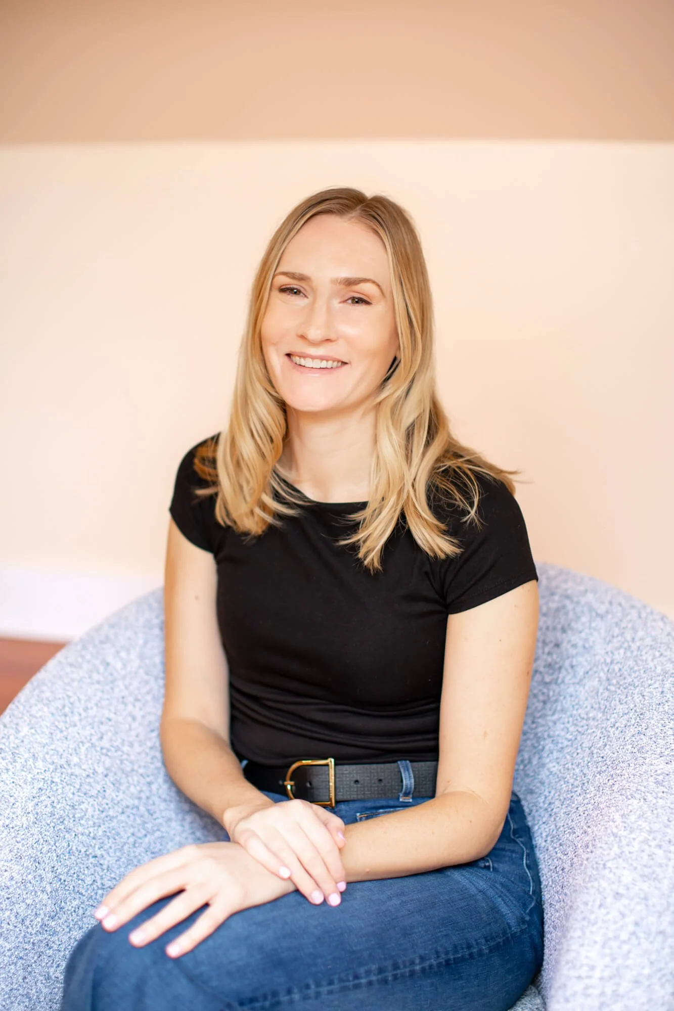 Santa Rosa therapist, Angela Sitka, LMFT, sitting in her private practice therapy office, sitting in a blue chair with yellow background, smiling wearing a black shirt