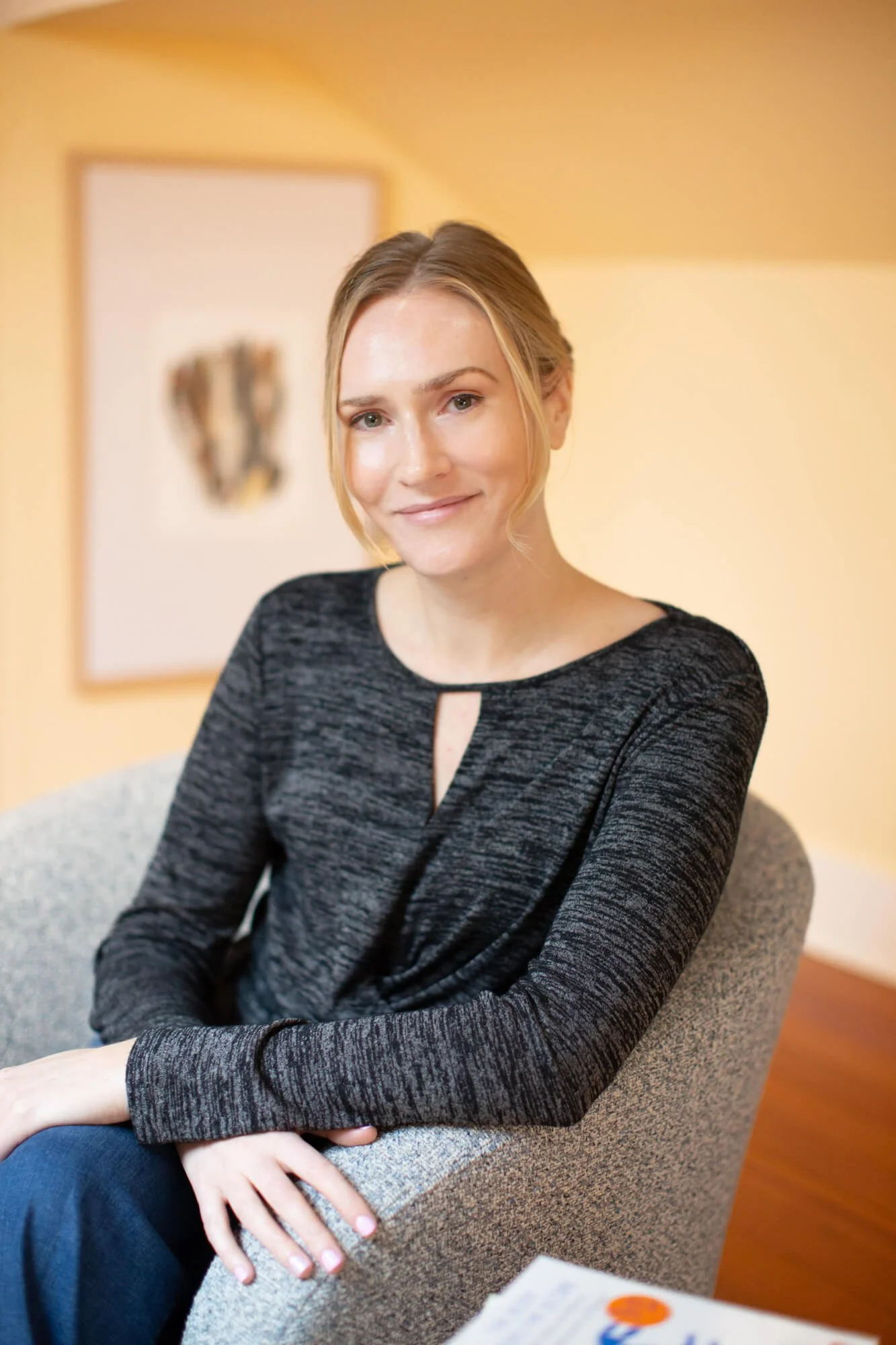 Angela Sitka, Licensed Marriage and Family Therapist in Santa Rosa, wearing a gray long-sleeve blouse sitting in chair, smiling and with arms crossed over lap.