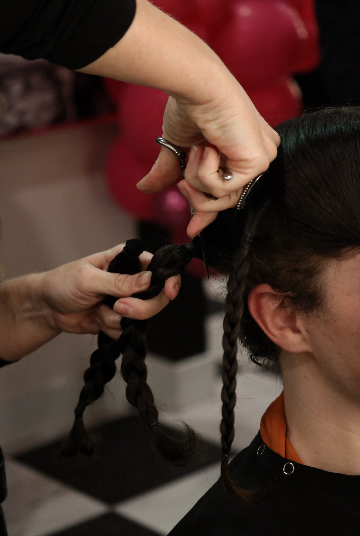 A person with long braided hair having the braid tied by a hairstylist.