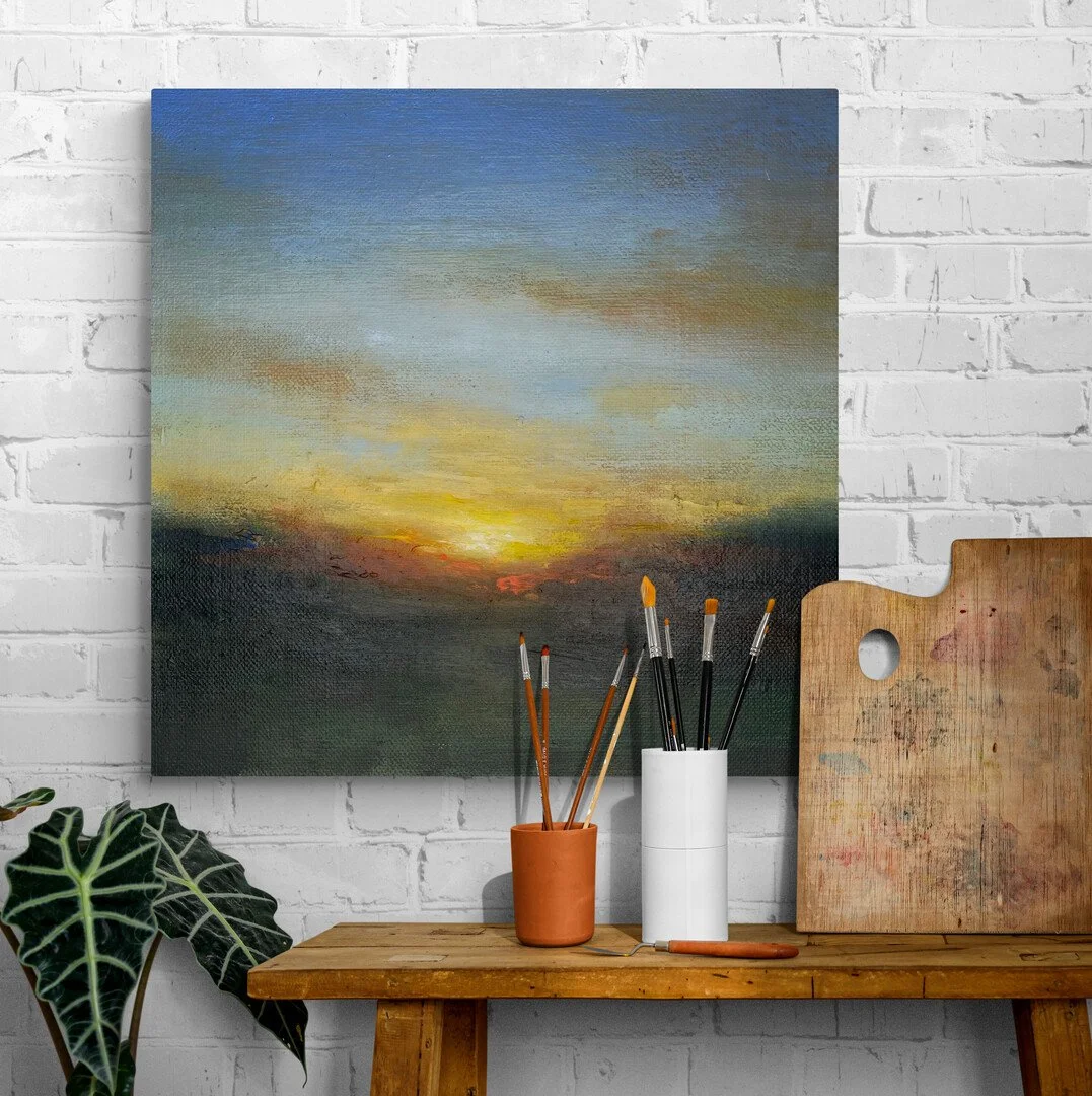 Gilded Sunset acrylic painting on wood hanging on studio wall above a table and plant, brushes and palette