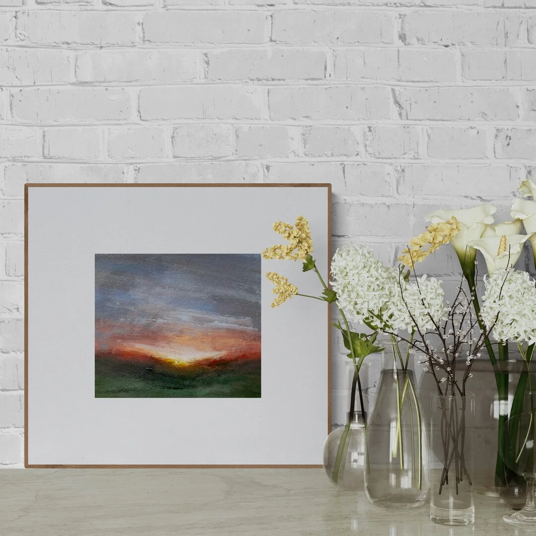 Small sunset on painting on paper framed and sitting on a shelf with vases of flowers