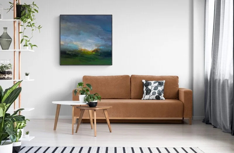 abstract landscape painting on canvas hanging above a brown sofa with coffee tables and plants in left corner