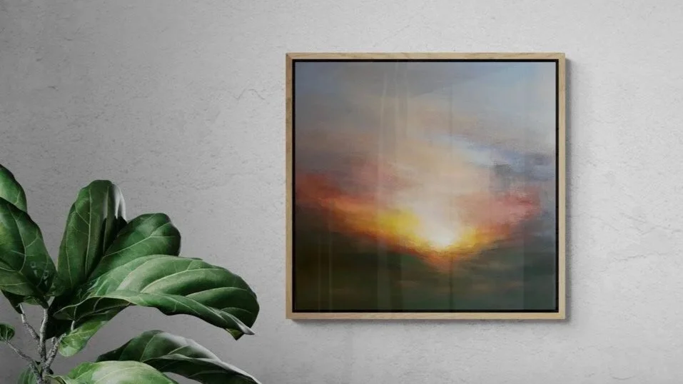 framed painting of a sunrise on the wall with part of a large plant showing in the lower corner