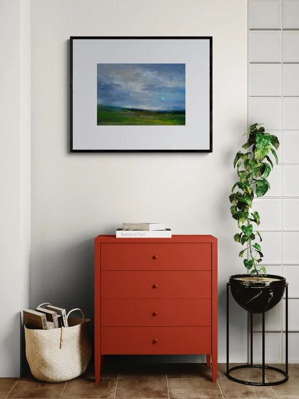 Daybreak on the Downs abstract landscape painting hanging on wall above a red cabinet and plant by Mary Burtenshaw