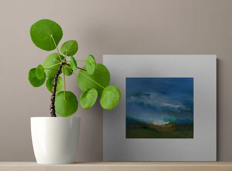 small abstract painting titled gentle showers mounted on a shelf with plant.