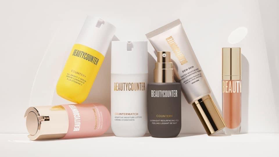 Collection of skincare products including bottles, tubes, and jars in pastel and neutral colors displayed on a white shelf.
