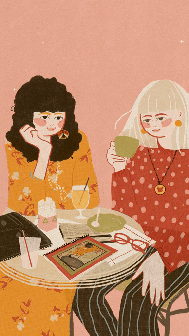 Two women sitting at a table with drinks, a magazine, and glasses, engaging in conversation against a pink background.