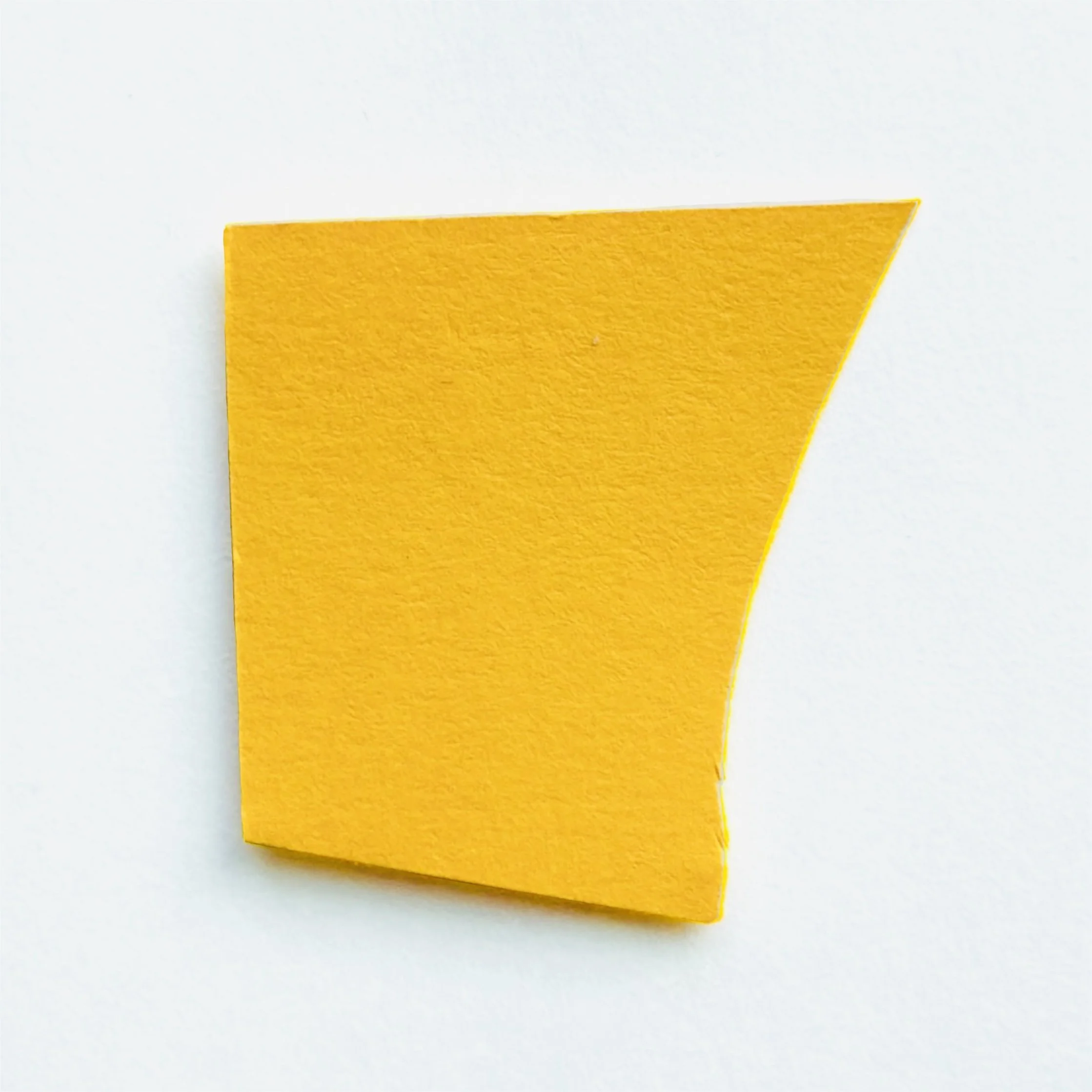 Yellow paper cut into a trapezoid shape with one curved edge, placed on a white background.