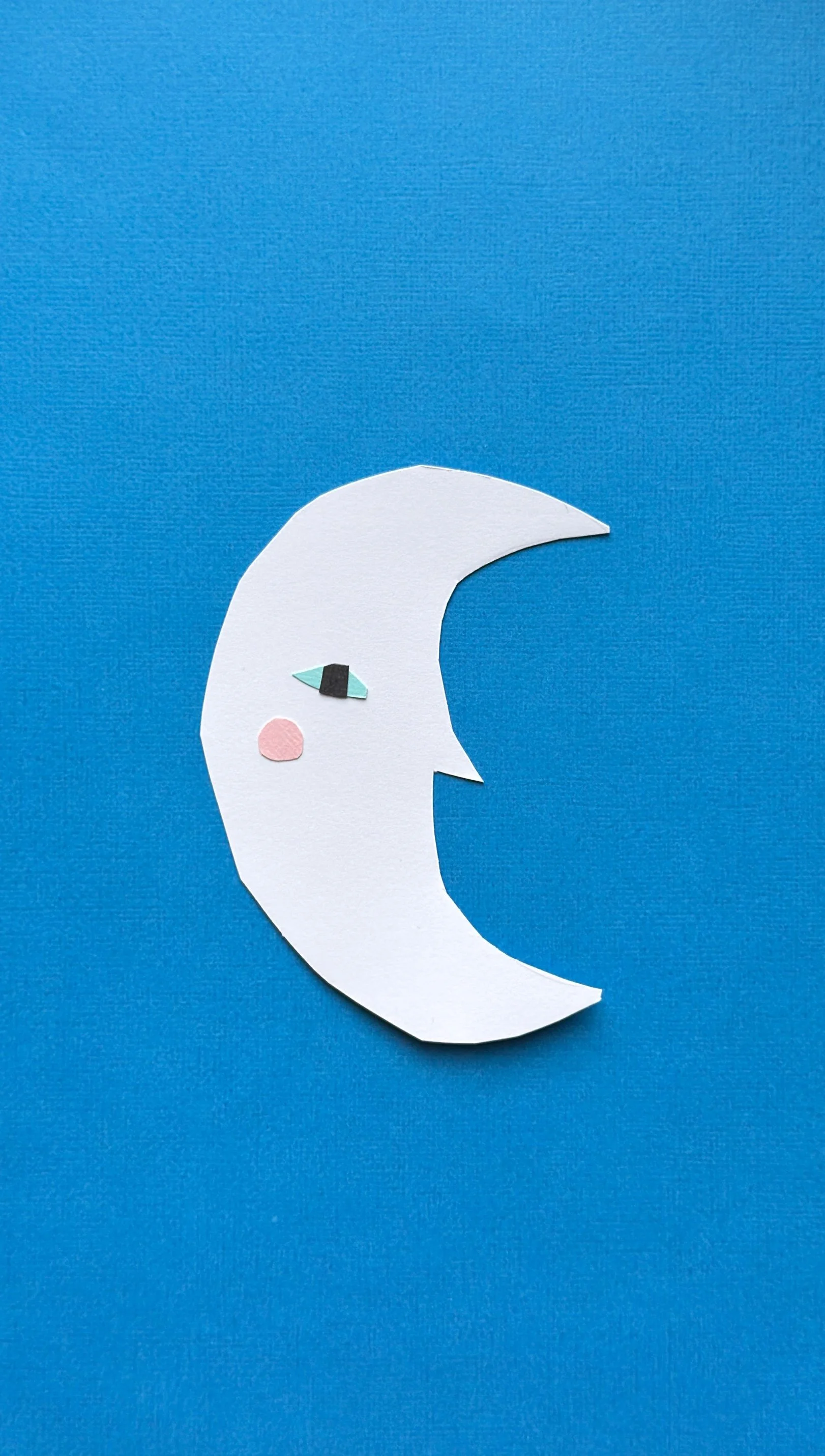 Paper craft moon with face on blue background.