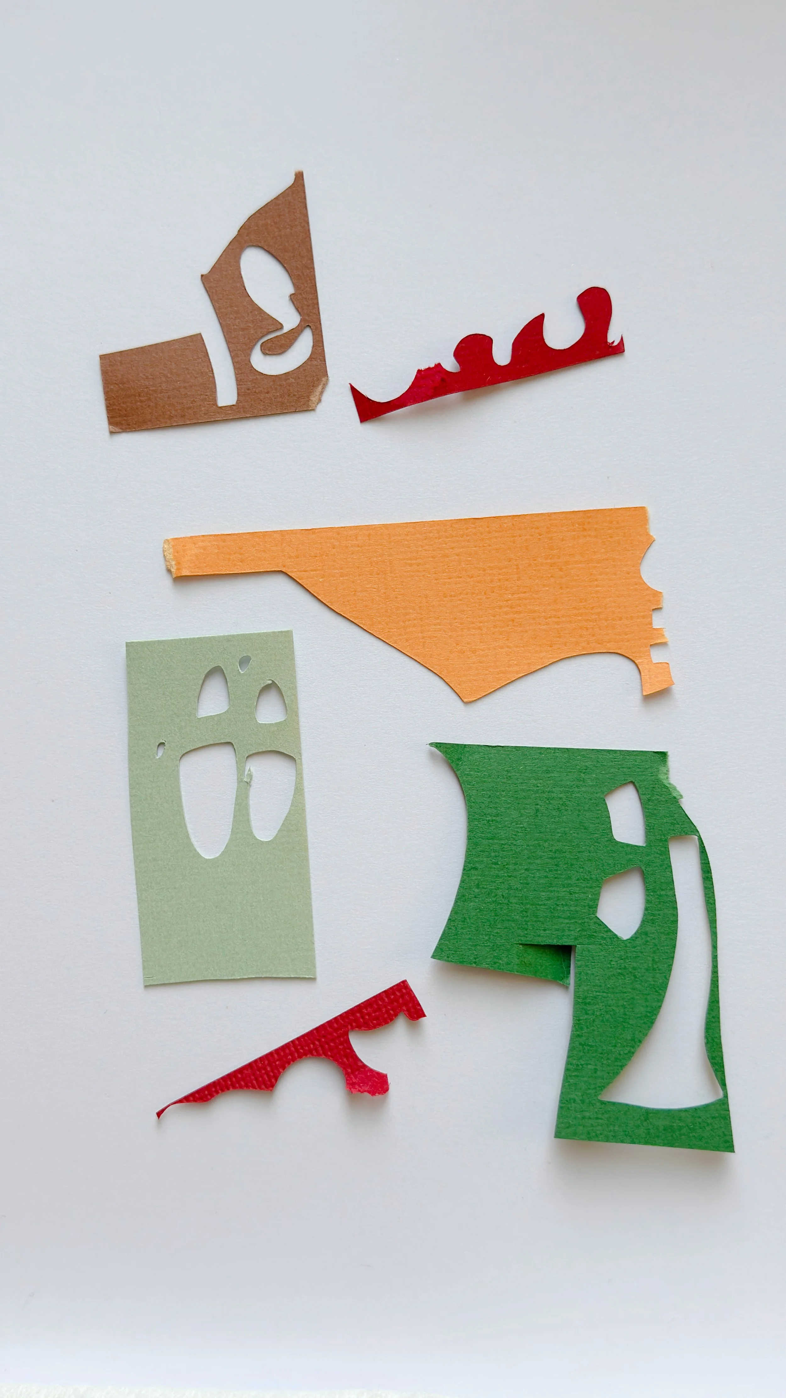 Paper scraps and color palette for a new hand-cut paper collage on a studio table.