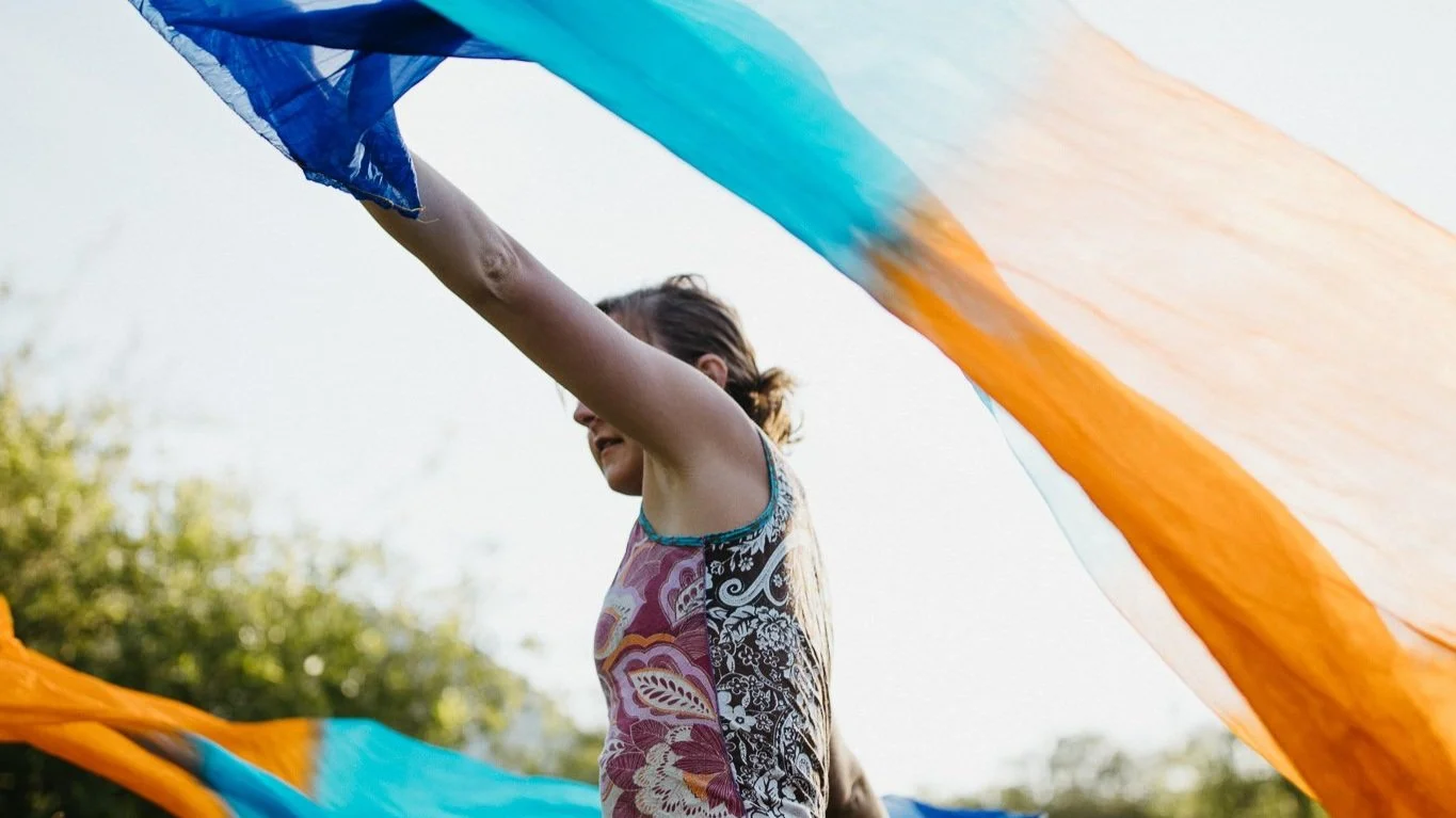 A woman holding colorful fabric outdoors on a bright day.