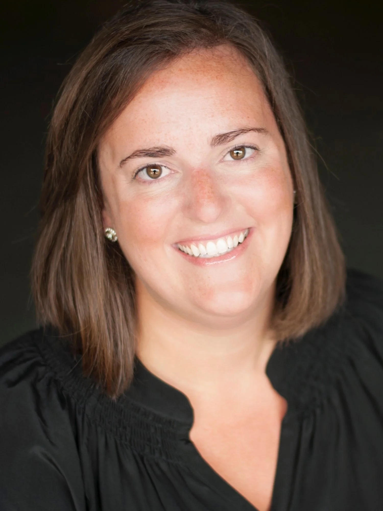 closely cropped headshot with soft lighting and a dark backdrop of a business woman