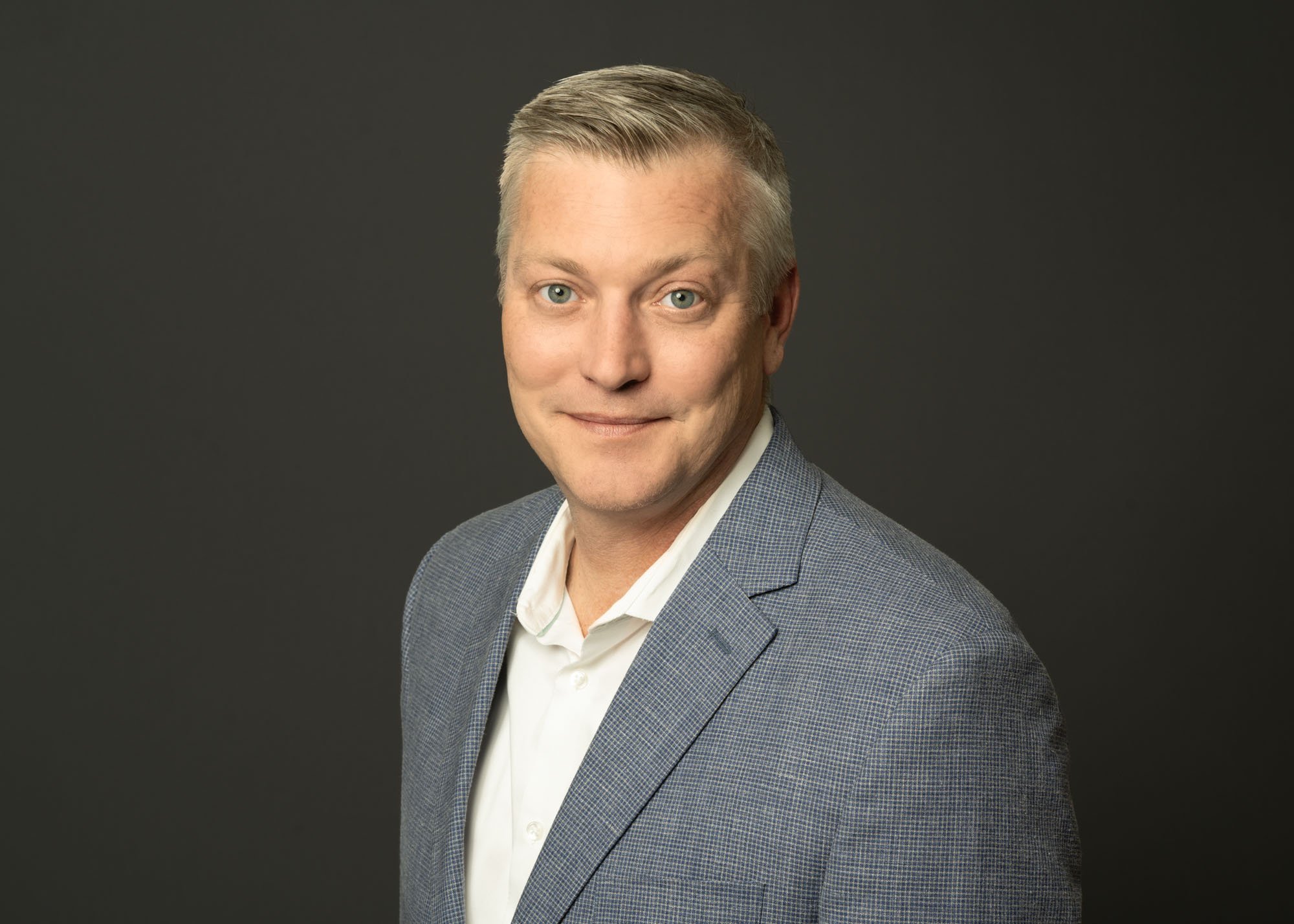 A headshot in Chicago of man with short grey hair posing slightly to the side wearing a white shirt and light grey jacket. This law partner is wearing professional attire as directed by the photographer. They prepared in advance of the photo shoot in
