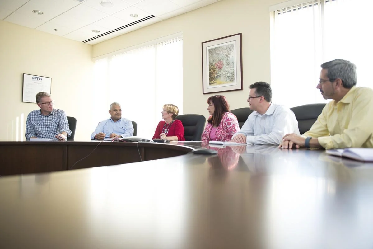 Six people sitting at a conference table in a meeting room, engaged in discussion.
