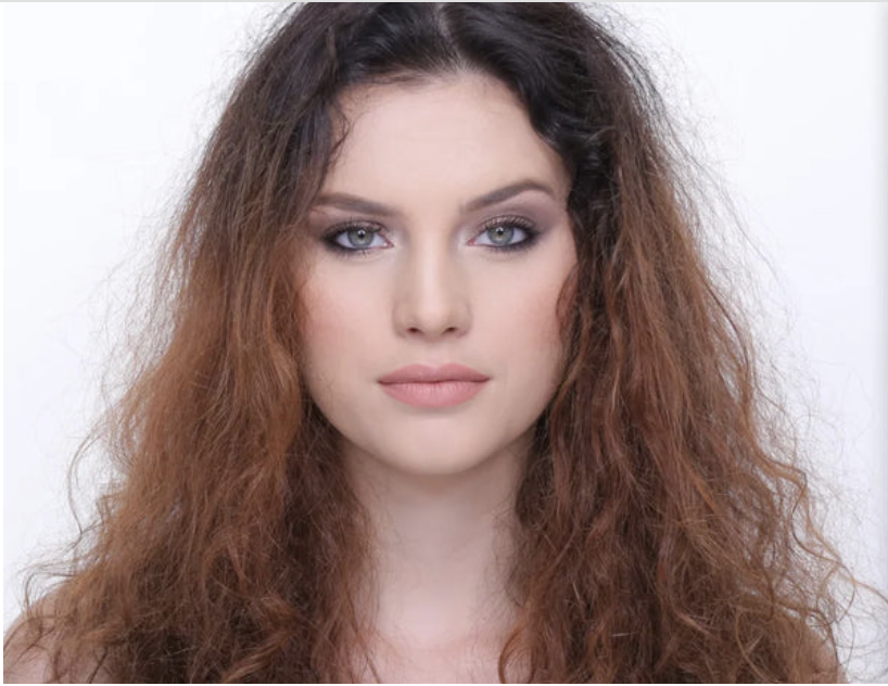 A young woman with curly, reddish-brown hair and light makeup looking directly at the camera.