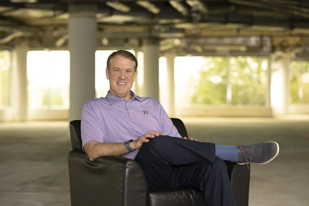 A Chicago photographer captured a portrait of a CEO inside of a warehouse. The environment is out of focus and the executive is in a chair smiling.
