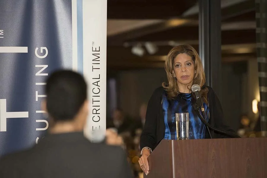 A woman speaking at a podium with a microphone, in front of a banner that reads 'E Critical Time'.