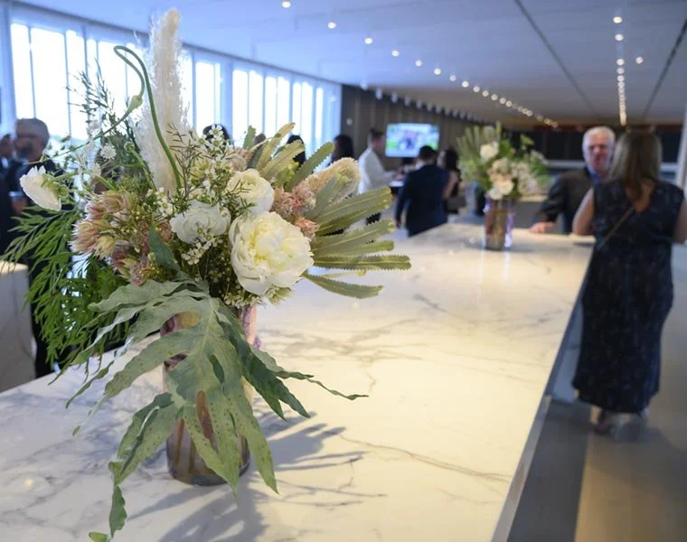 Flowers in a vase on a marble counter in a modern indoor space with people in the background during a corporate event.