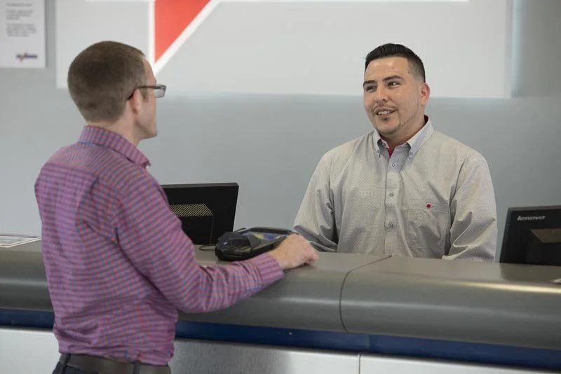 Two men at a reception desk having a conversation in an office setting.